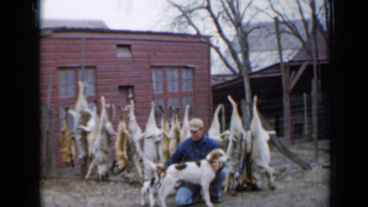 Hunter pets a white and brown dog with hanging pelts behind him.