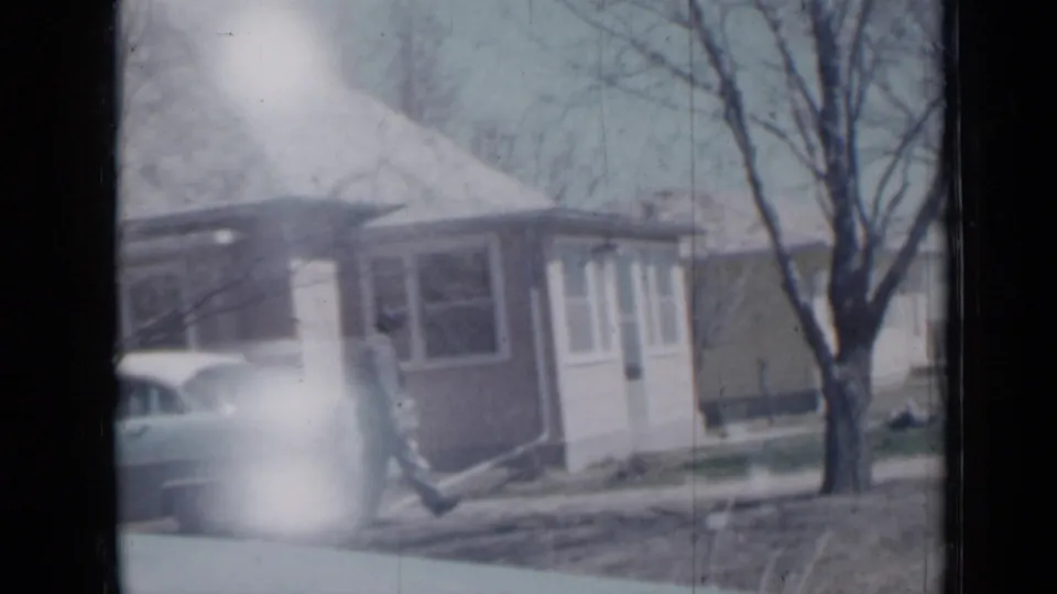 1958 Minnesota 8mm frame showing a small house exterior, an older car, a leafless tree, and a person in the yard.