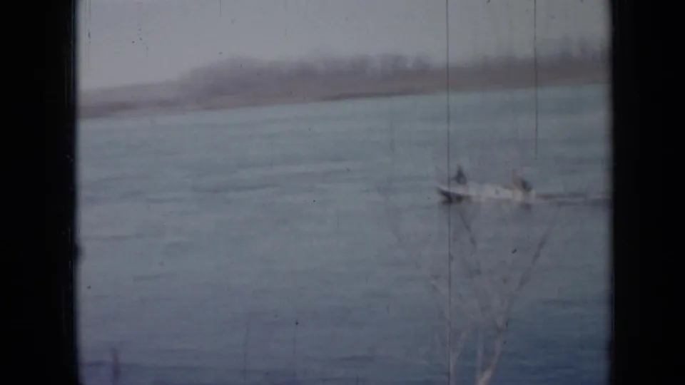 1958 Minnesota home-movie frame of a small boat with two distant occupants on a muted blue-gray lake.