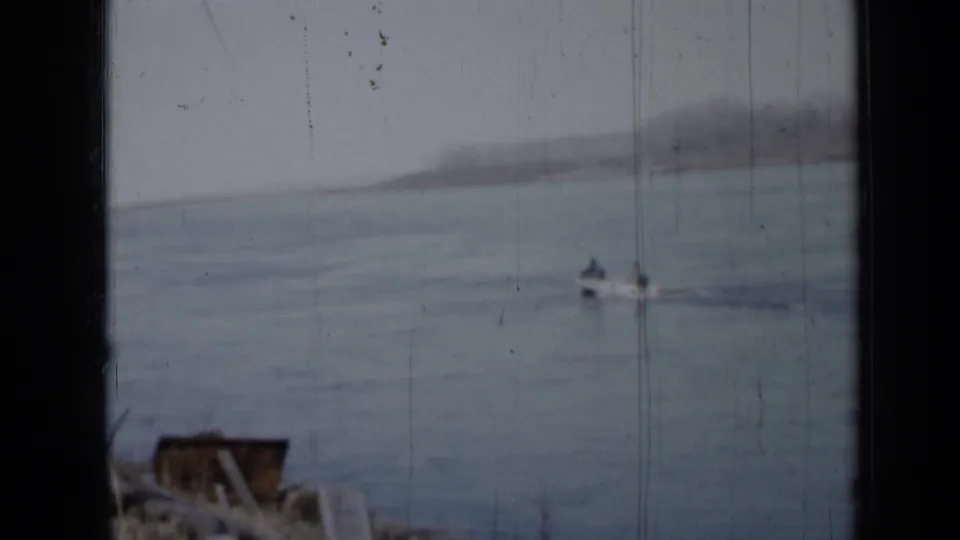 1958 Minnesota 8mm frame showing a distant two-person boat leaving a faint wake across calm lake water.