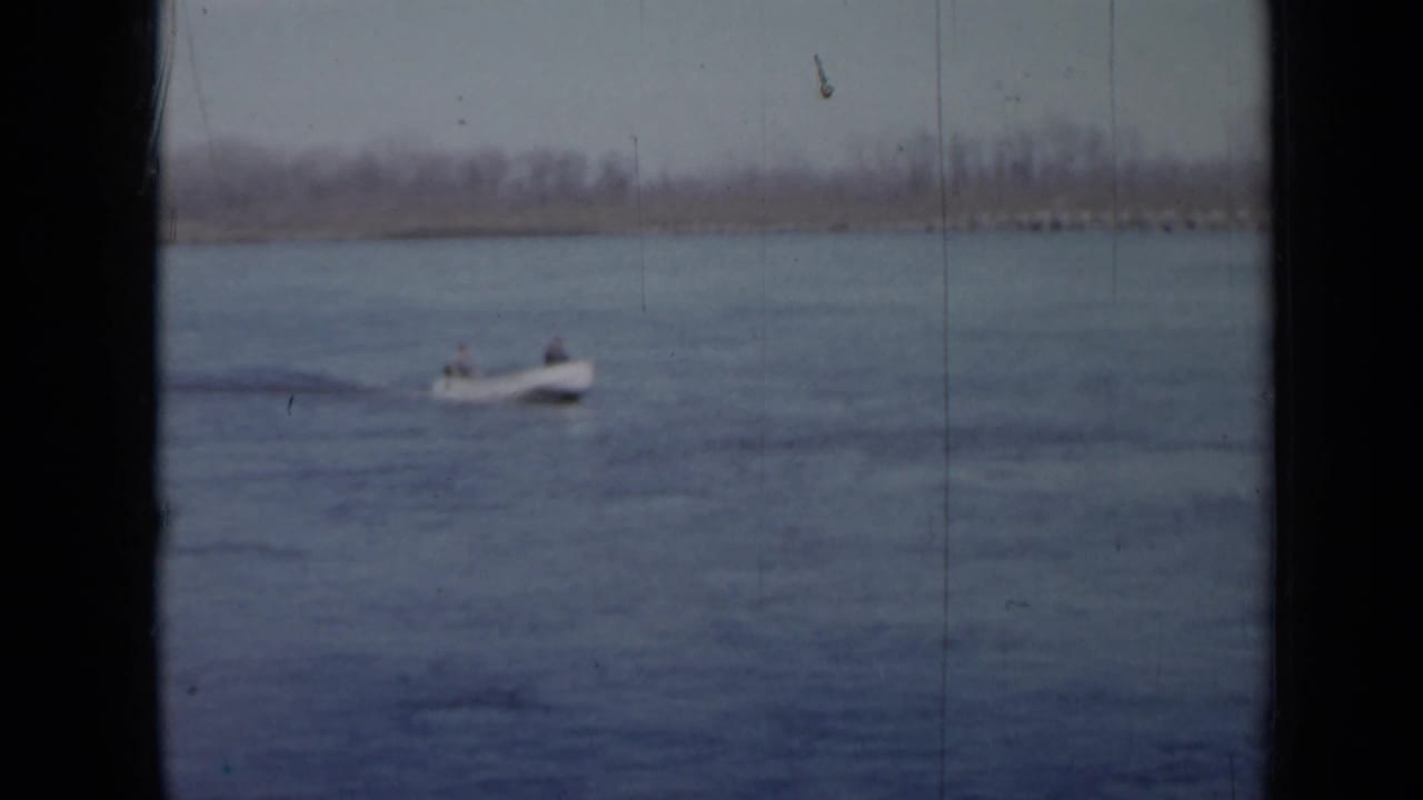 Small motorboat crossing a calm lake with two people aboard.