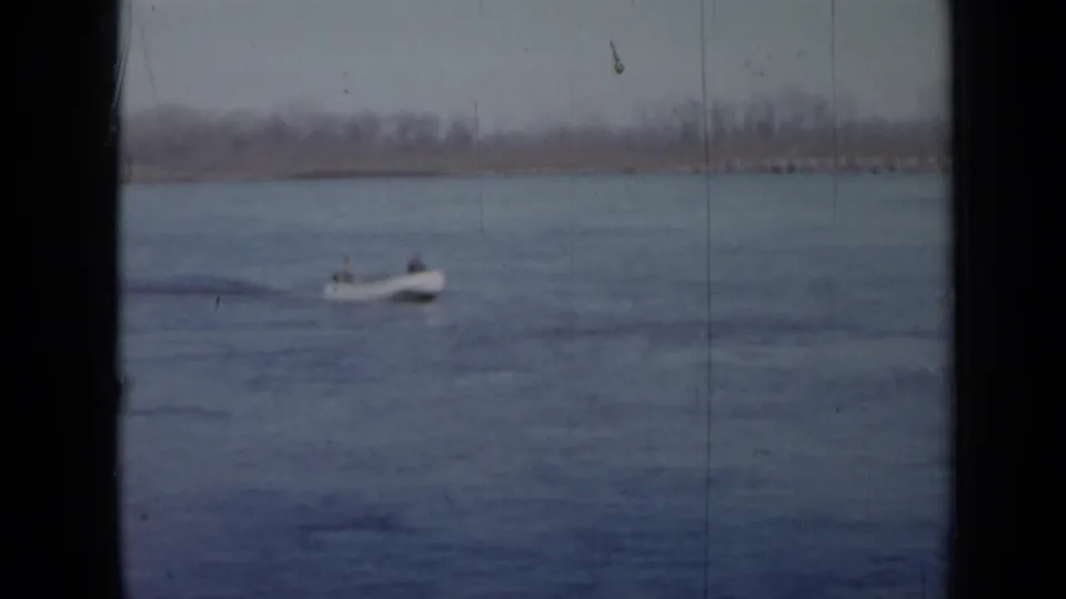 1958 Minnesota 8mm frame showing a small motorboat with two people moving across calm lake water.