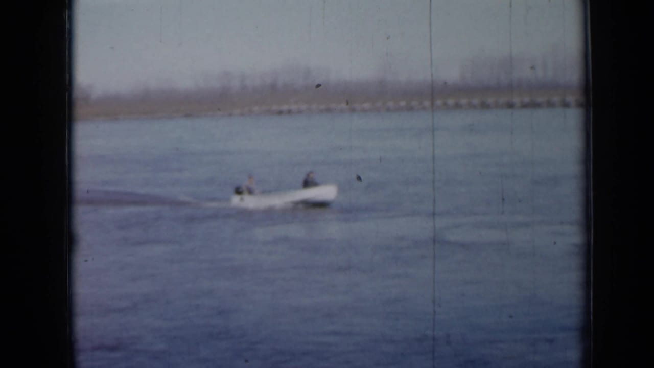 Motorboat with two occupants moving across open water near a distant shoreline.