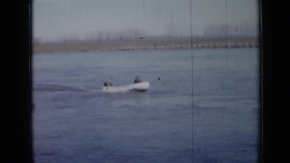 A small boat with two people aboard moves across a Minnesota lake in this 1958 home-movie frame.