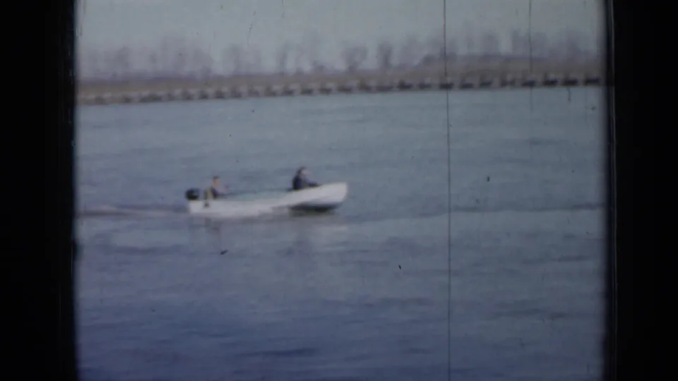 Two people ride in a small white motorboat on a Minnesota lake, filmed on 8mm in 1958.