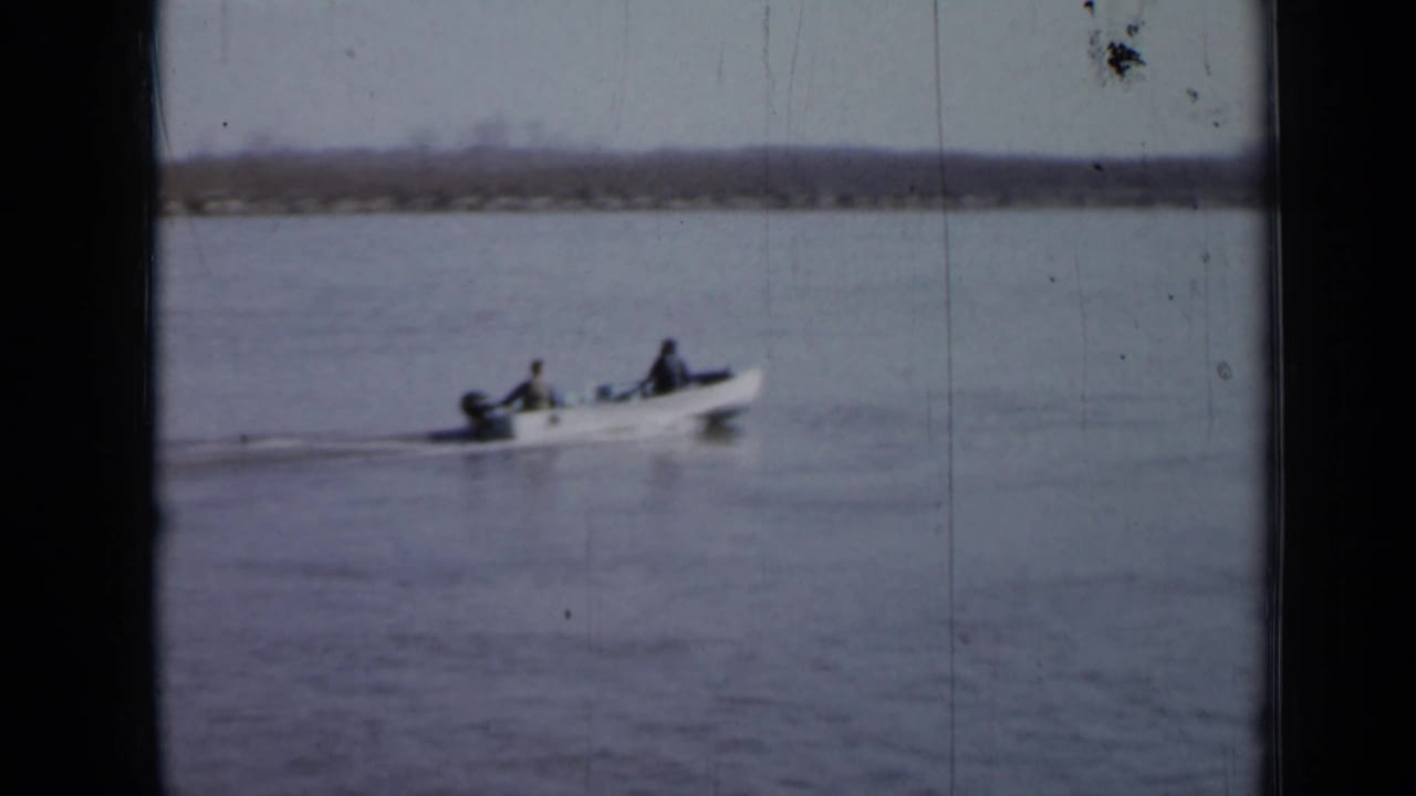Small outboard motorboat continues across open water with two men aboard.