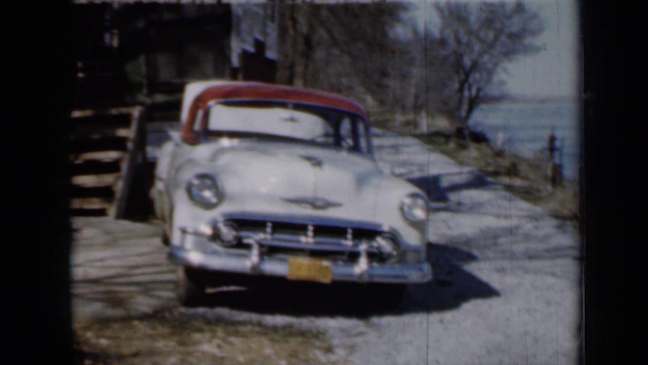 A pale 1950s Chevrolet with a red roof sits near rustic wooden steps in the stated Minnesota cabin setting.