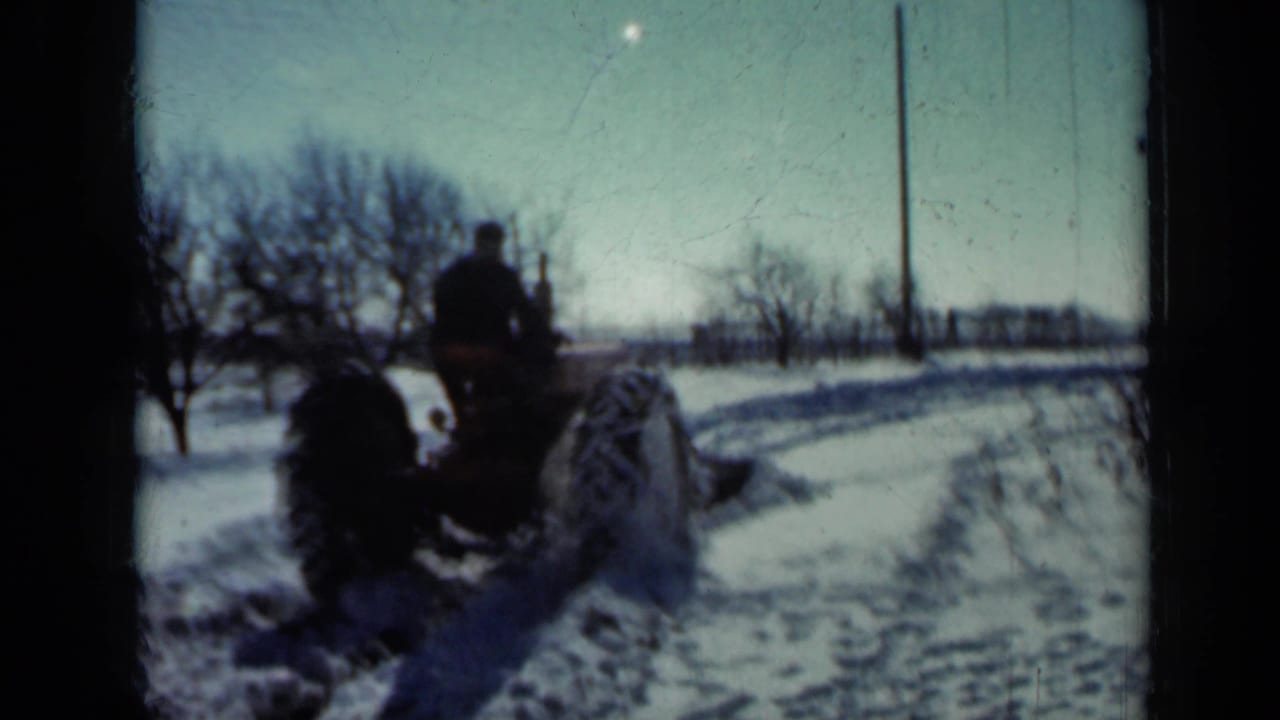Rear view of a tractor plowing snow beside a rural road.