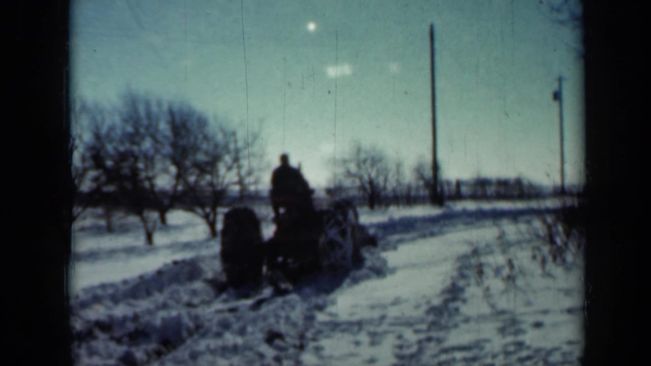 Man driving a tractor through a snow-covered rural field.
