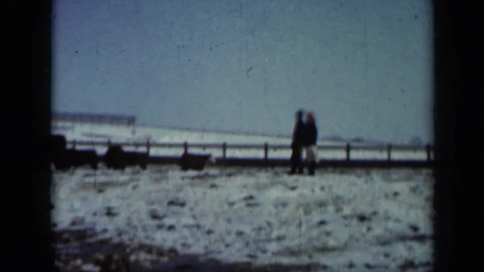 Distant figures in a snowy 1958 Minnesota pasture watch livestock near a long rural fence line.