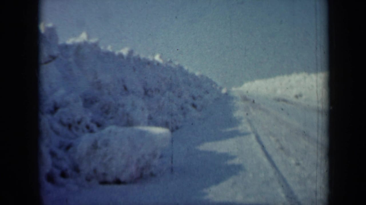 Snow-covered road bordered by high drifts under a pale blue sky.