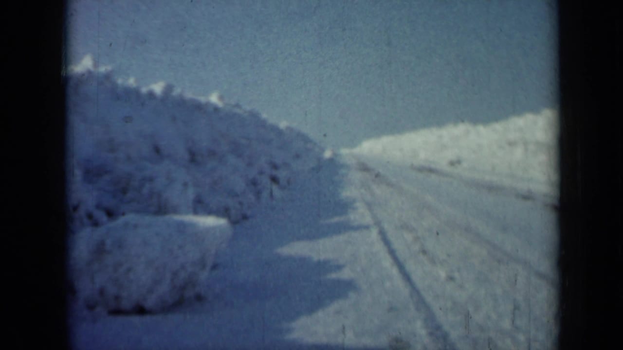 1958 Minnesota frame looking ahead along a plowed winter road, with tall snowbanks and no visible people or vehicles.