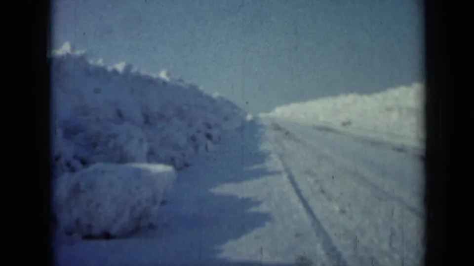 1958 Minnesota frame looking ahead along a plowed winter road, with tall snowbanks and no visible people or vehicles.