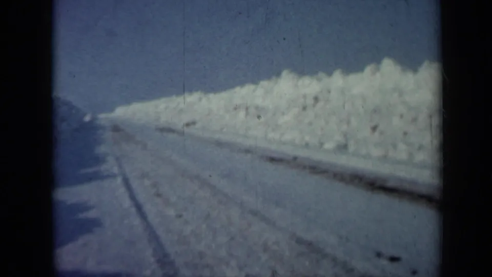 1958 Minnesota winter frame showing a deserted plowed road beside a tall sunlit snowbank, with no visible people, vehicles, or signs.