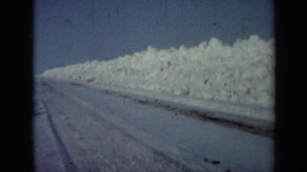 Snow-covered farm road or pen edge with a long bank of snow and dark tire tracks.
