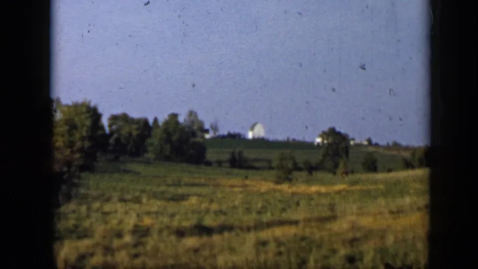1959 Aledo, Texas 8mm frame showing open grassland, trees, and a distant white house or barn on a low hill.