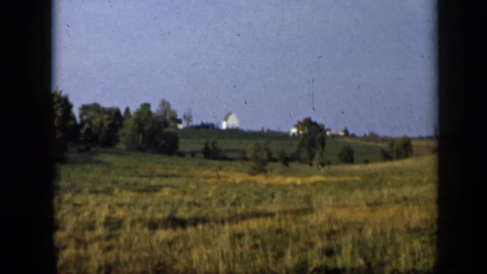 Aledo, Texas home-movie view of rolling green fields, scattered trees, and distant light-colored buildings along the horizon.