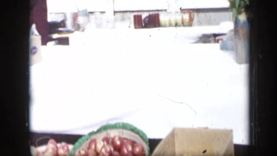 Overexposed home-movie frame, likely near a yard or porch, with red chairs and a basket of onions visible at the lower edge.