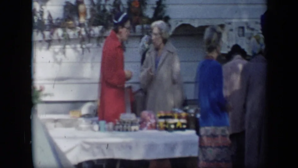 Aledo, Texas 1959 frame showing two women conversing beside an outdoor table while other women stand nearby.