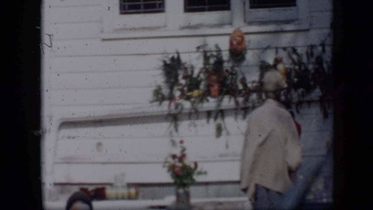 A woman in a hat walks past a flower display mounted by a white building.
