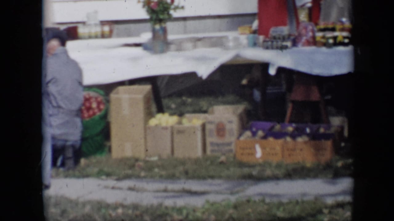 Outdoor sale table with boxes of goods and a person seated near the left edge.