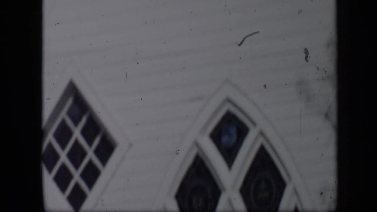 1959 Aledo, Texas home-movie frame showing white clapboard siding and pointed Gothic-style windows in soft focus.