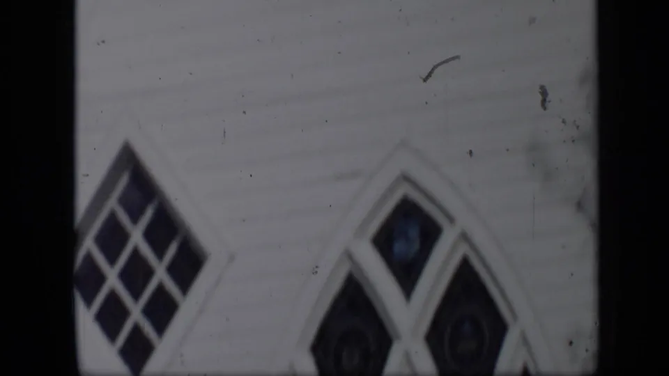 1959 Aledo, Texas home-movie frame showing white clapboard siding and pointed Gothic-style windows in soft focus.