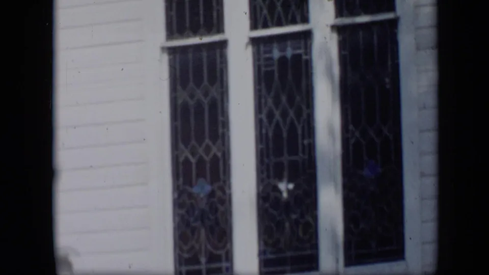 1959 Aledo, Texas home-movie view of tall patterned windows on a white clapboard building exterior.