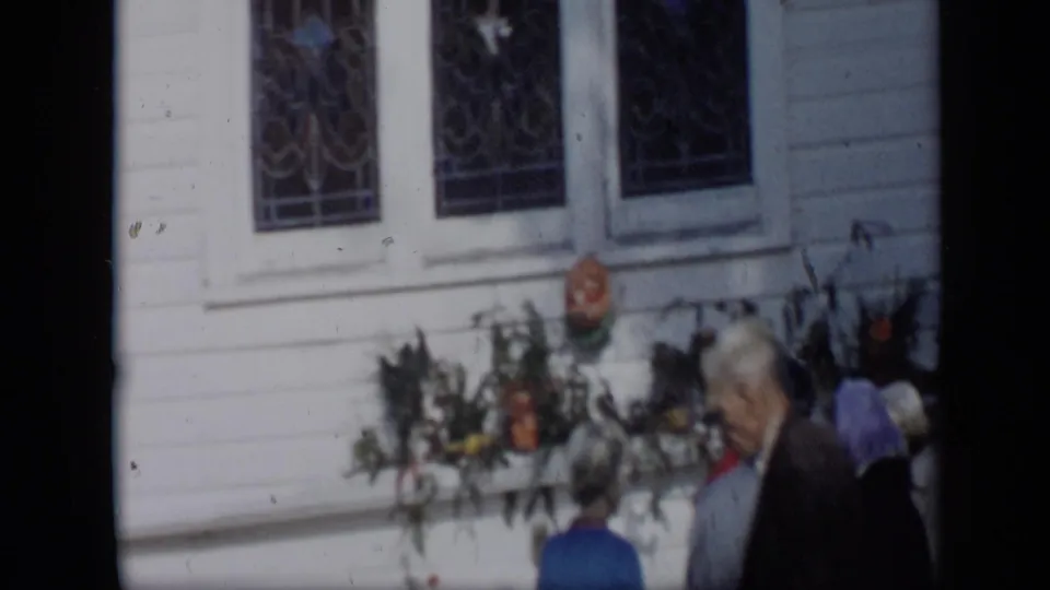 1959 Aledo, Texas frame showing people near a white clapboard church-like building with Gothic windows and flowers.