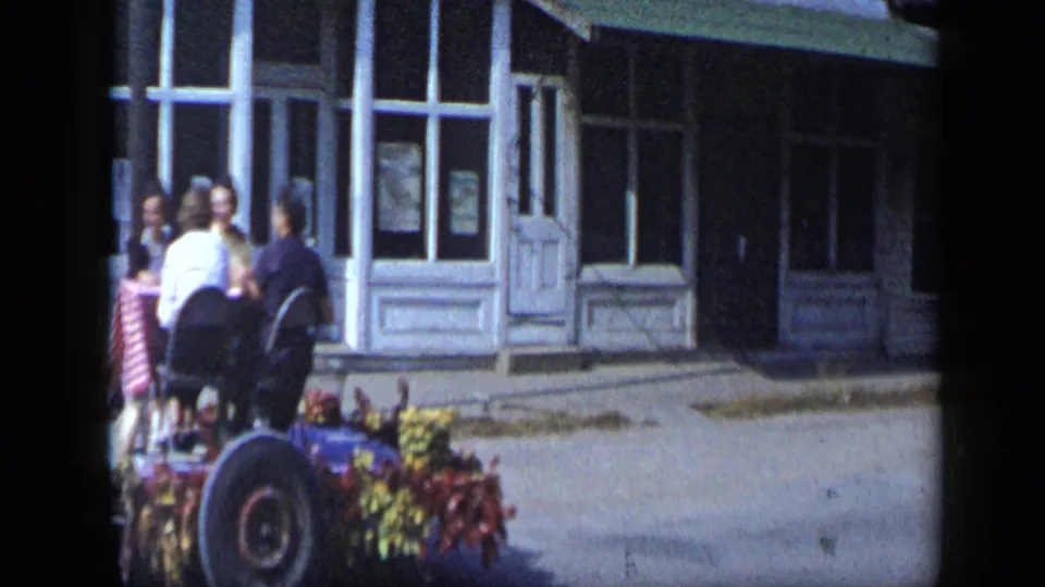 Aledo parade float detail with women seated and standing near a table as the tractor-pulled float continues along the street.