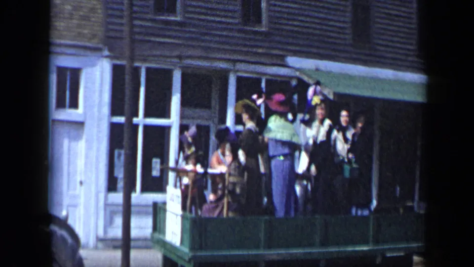 A second Aledo, Texas parade float shows women in vintage costumes and hats gathered on a green platform in daylight.