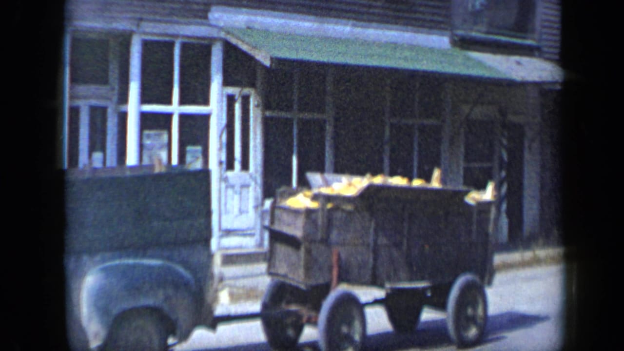 Wooden produce wagon beside storefront windows on a town street.