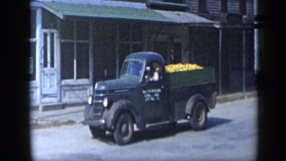 Aledo, Texas 1959 home-movie frame showing a black pickup truck with yellow produce in the bed and a driver visible in the cab.