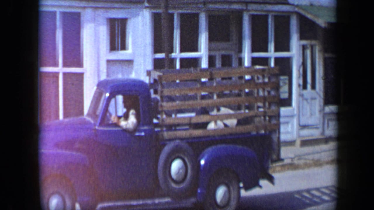 Dark blue pickup with wooden stake sides passing storefront windows.