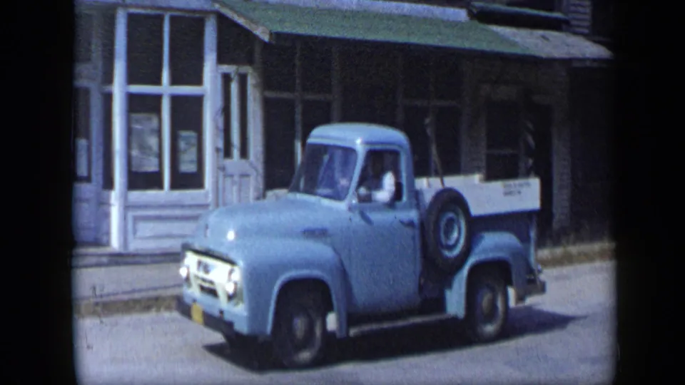 A 1959 Aledo, Texas street view shows the light blue pickup near white storefronts, with the driver visible in profile.