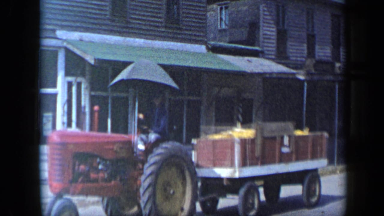 The tractor and wooden wagon continue past a storefront in the 1959 Aledo, Texas home-movie scene.