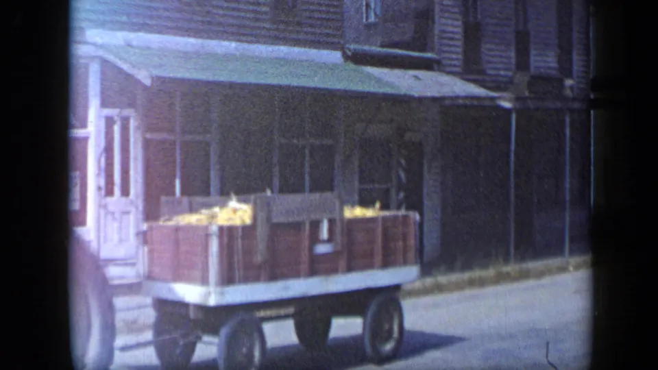 The wooden wagon of produce remains in view as the tractor moves out of frame on a small-town Aledo street in 1959.