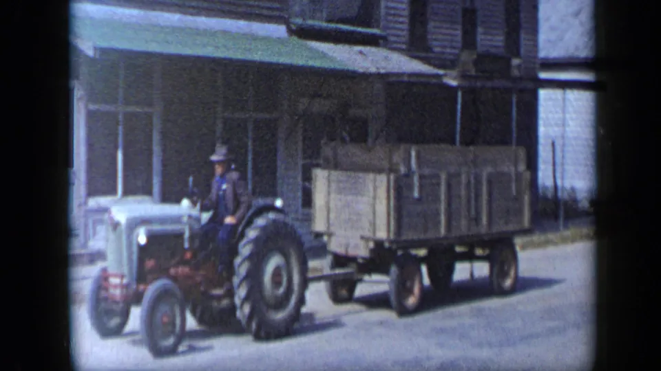 A closer 8mm frame shows the tractor driver in a hat towing a wooden wagon along the town street in 1959 Aledo, Texas.