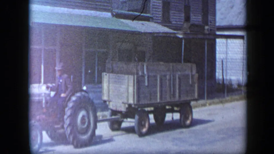The wooden wagon follows the tractor toward the edge of the frame, with storefronts and a quiet street behind it in Aledo, Texas.