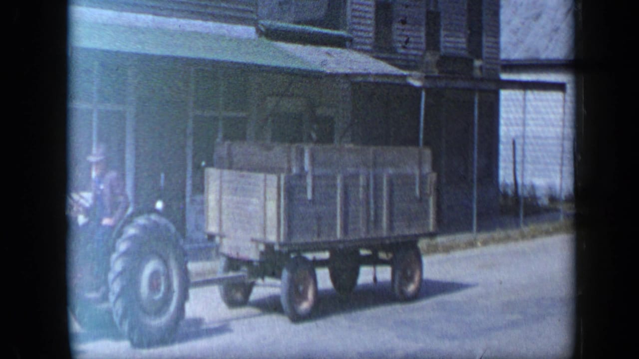 Tractor pulling a wooden trailer along a small-town street.