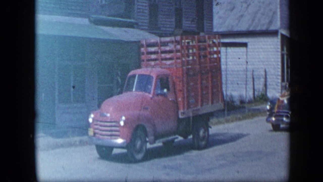 Aledo, Texas 1959 frame with a red mid-century truck fitted with a wooden crate bed near low streetfront buildings.