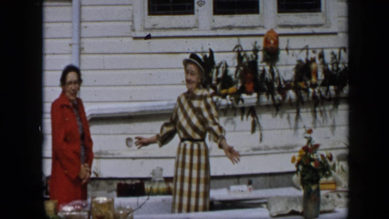 In Aledo, Texas, 1959, two women stand near a display table outside a white clapboard house with jars, flowers, and fall decor.