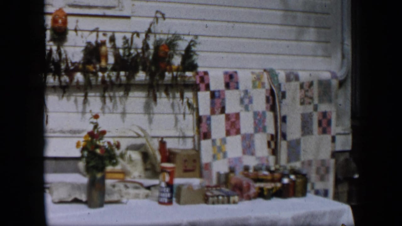 Aledo, Texas 1959 frame of a porch table with flowers, patterned cloth, cardboard boxes, and small household containers.