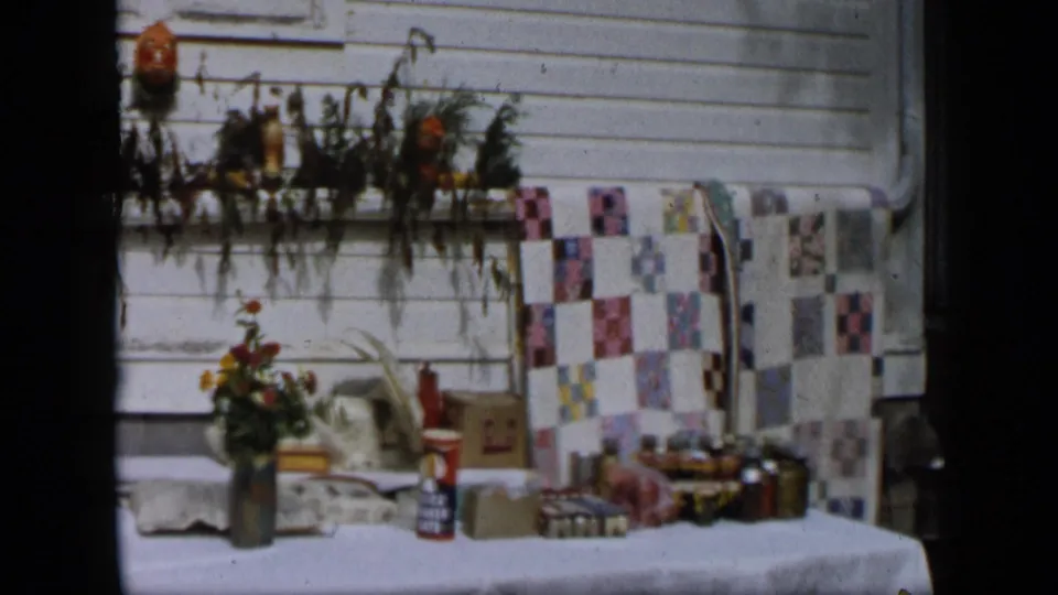 Aledo, Texas 1959 frame of a porch table with flowers, patterned cloth, cardboard boxes, and small household containers.