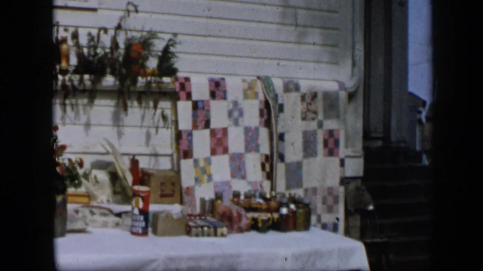 Aledo, Texas 1959 home-movie frame showing a porch display, patterned fabric, flower vase, boxes, and a doorway.