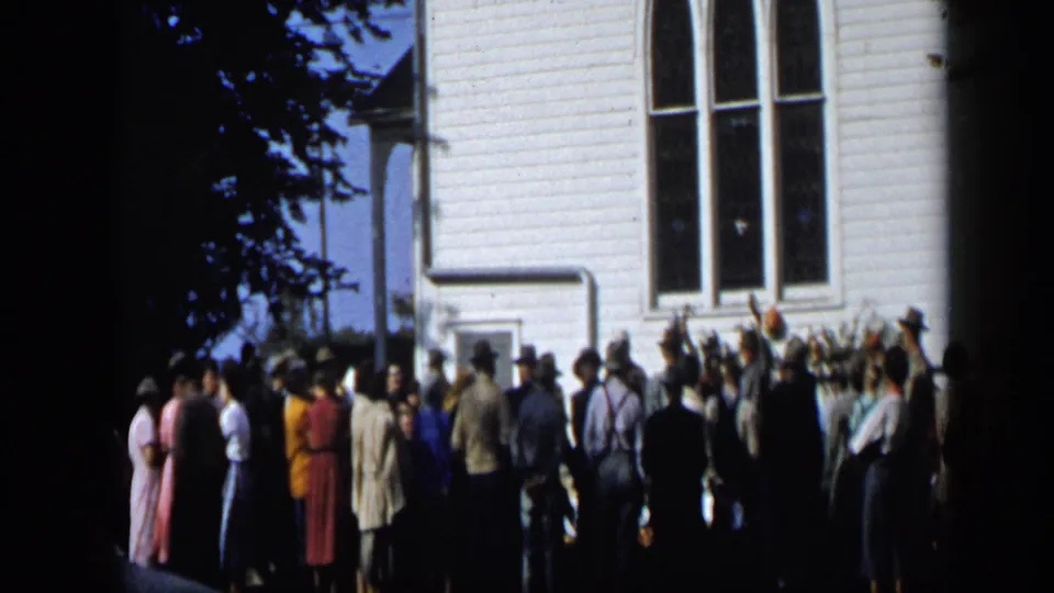 Aledo, Texas 1959 home-movie frame showing people gathered outside a white clapboard building in bright daylight.