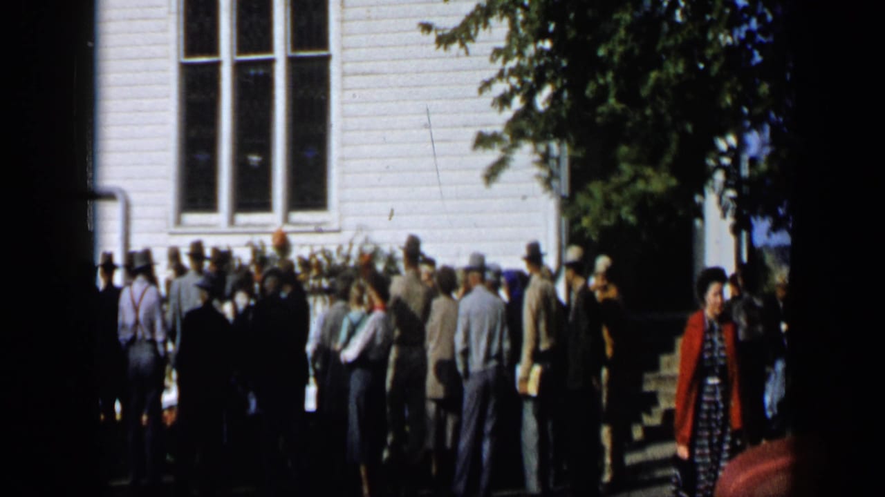 Crowd of people gathered outside a white clapboard building during a parade.