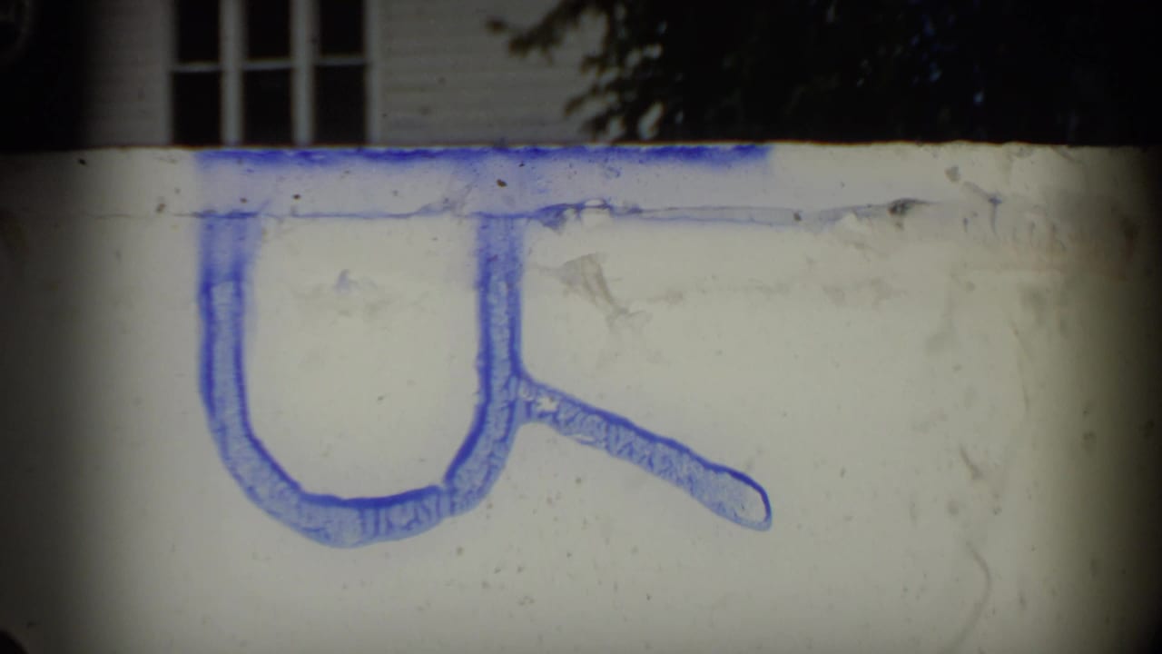 A brief film leader or marked frame appears, with a blue hand-drawn shape on a pale background between parade shots.