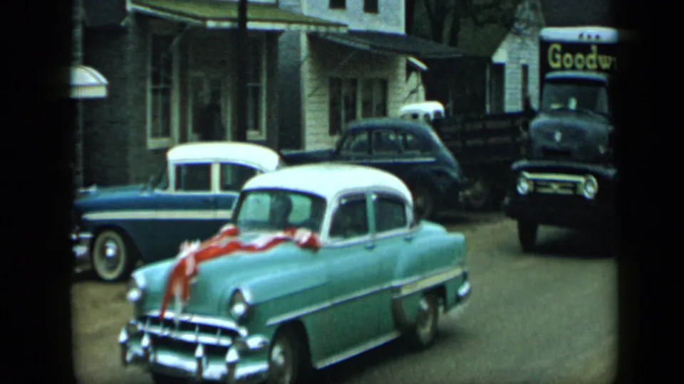 Ribboned light green car on an Aledo street with a two-tone sedan, dark sedan, pickup, and visible Goodwill truck sign behind it.