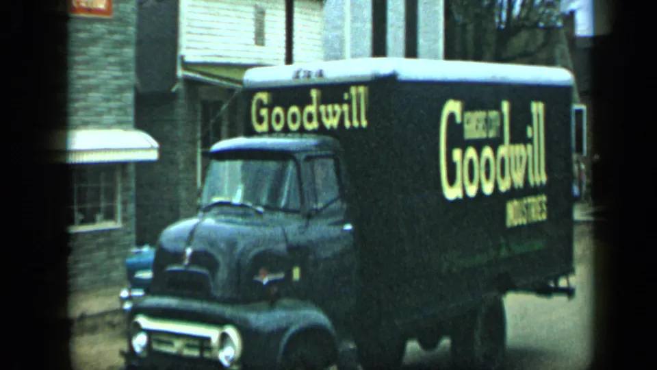 Black Goodwill Industries truck with large yellow lettering passes along an Aledo, Texas street in 1959 home-movie footage.